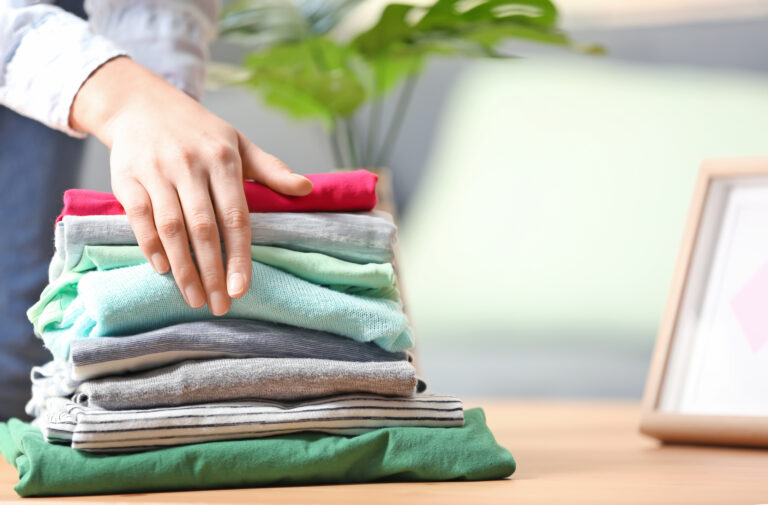 Woman putting stack of clean clothes after laundry on table